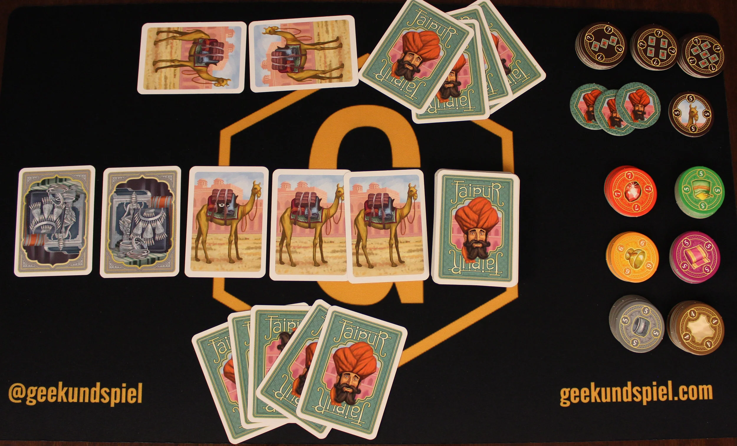 Game setup. Notice how the bottom player has no camels, but the top player is starting with two. The chips for sold cards are on the right, the bonus chips are at the top, and the three green chips with the person's face are given out for each round one.