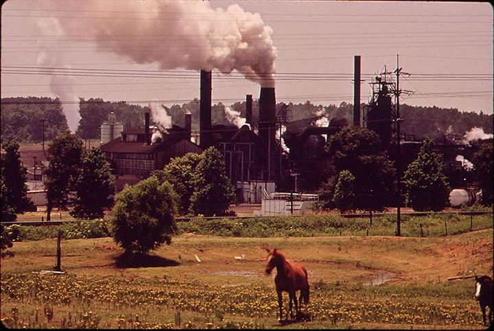 Caption: The Atlas Chemical Company belches smoke across pasture land in foreground. It is referred to disparagingly in the community because black soot from the plant covers everything nearby. Photographer: Marc St. Gil Date Created: 1973 May