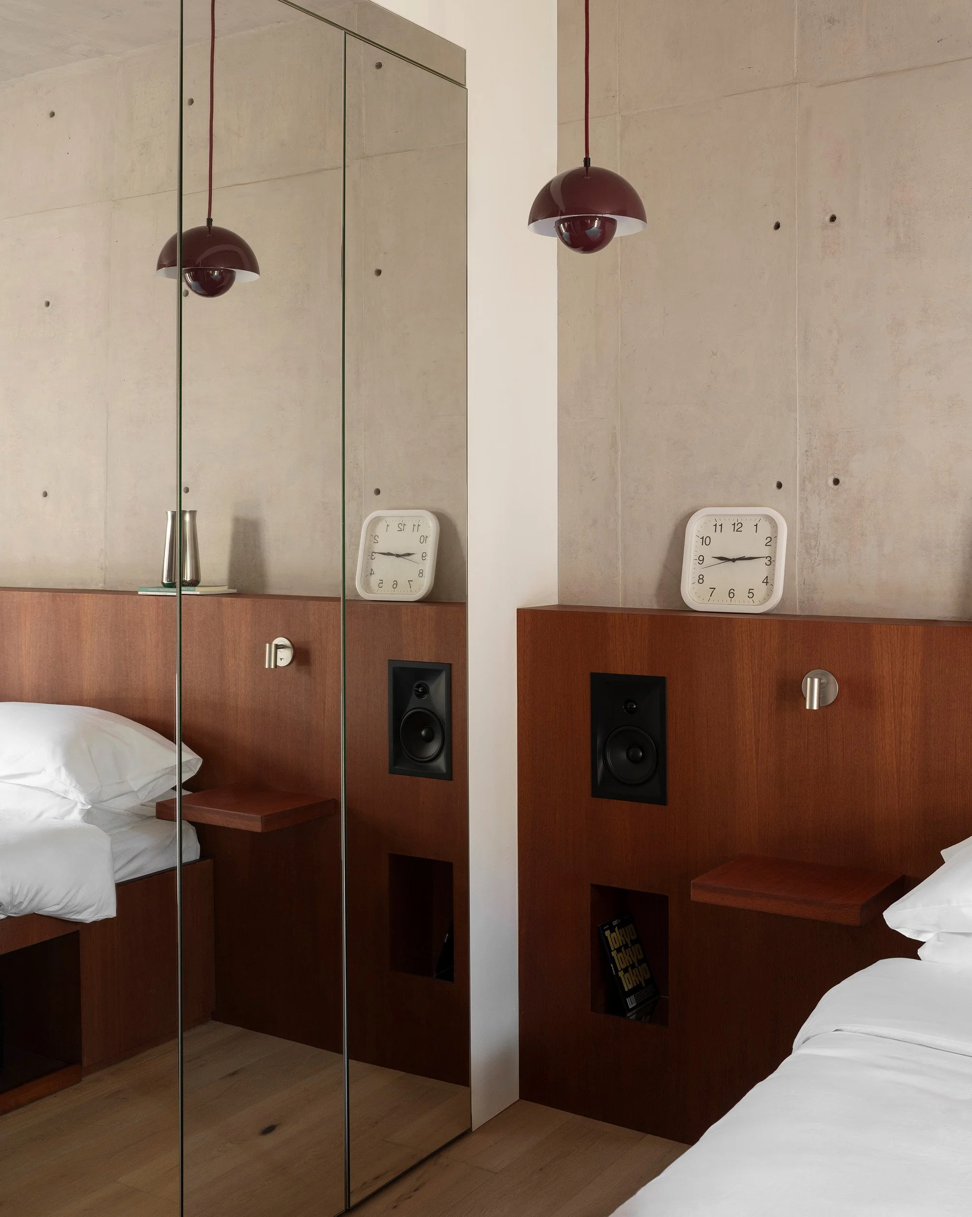 Minimalist bedroom featuring a custom wood headboard with built-in speakers seen through slatted screen doors at San Luis Airbnb in Mexico City, interior design by Mariel Lozano Studio, photo by Fabian Martinez.