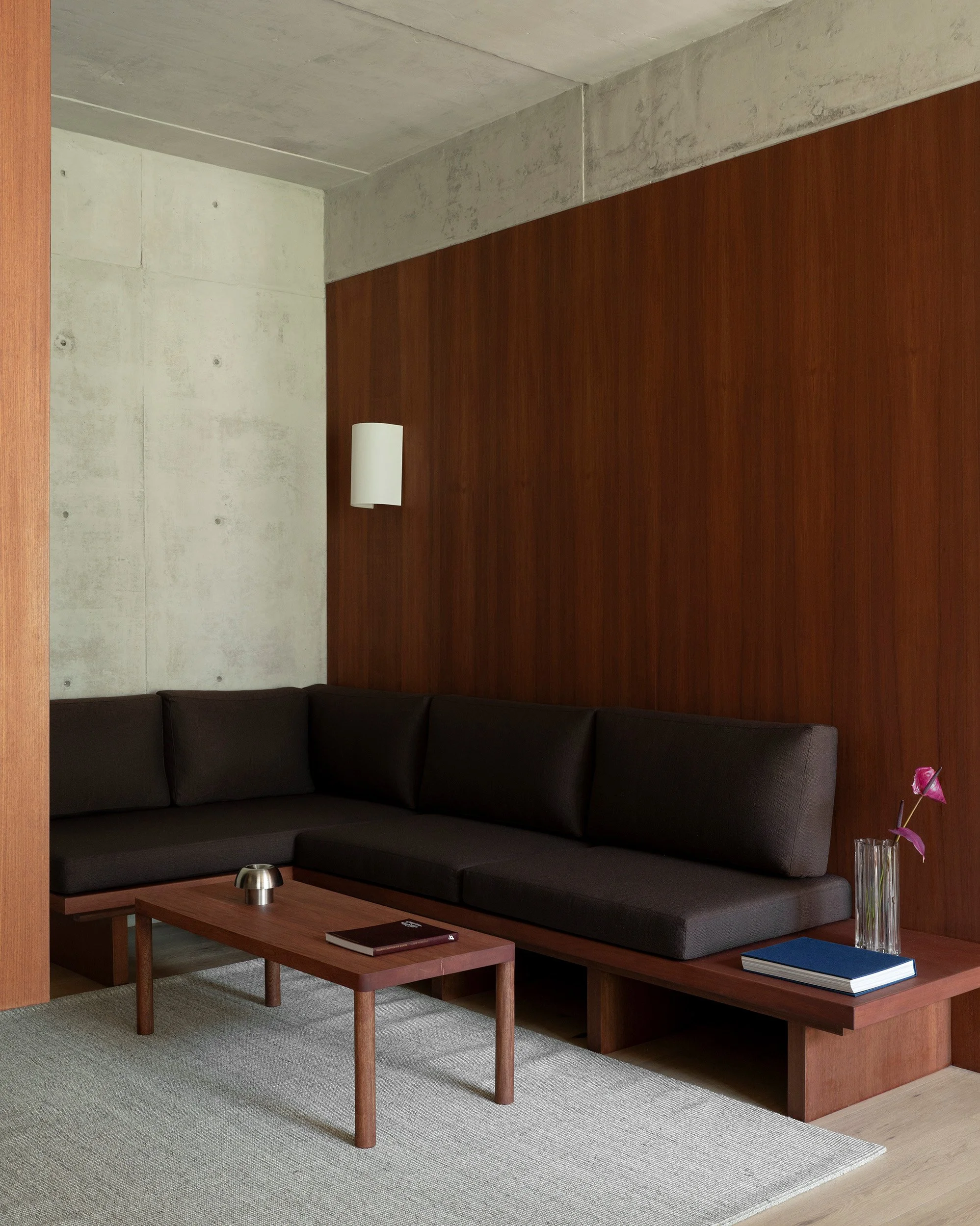 Minimalist living area showcasing a custom wooden banquette bench, low coffee table, and wood paneling at San Luis Airbnb in Mexico City, designed by Mariel Lozano Studio, photo by Fabian Martinez.