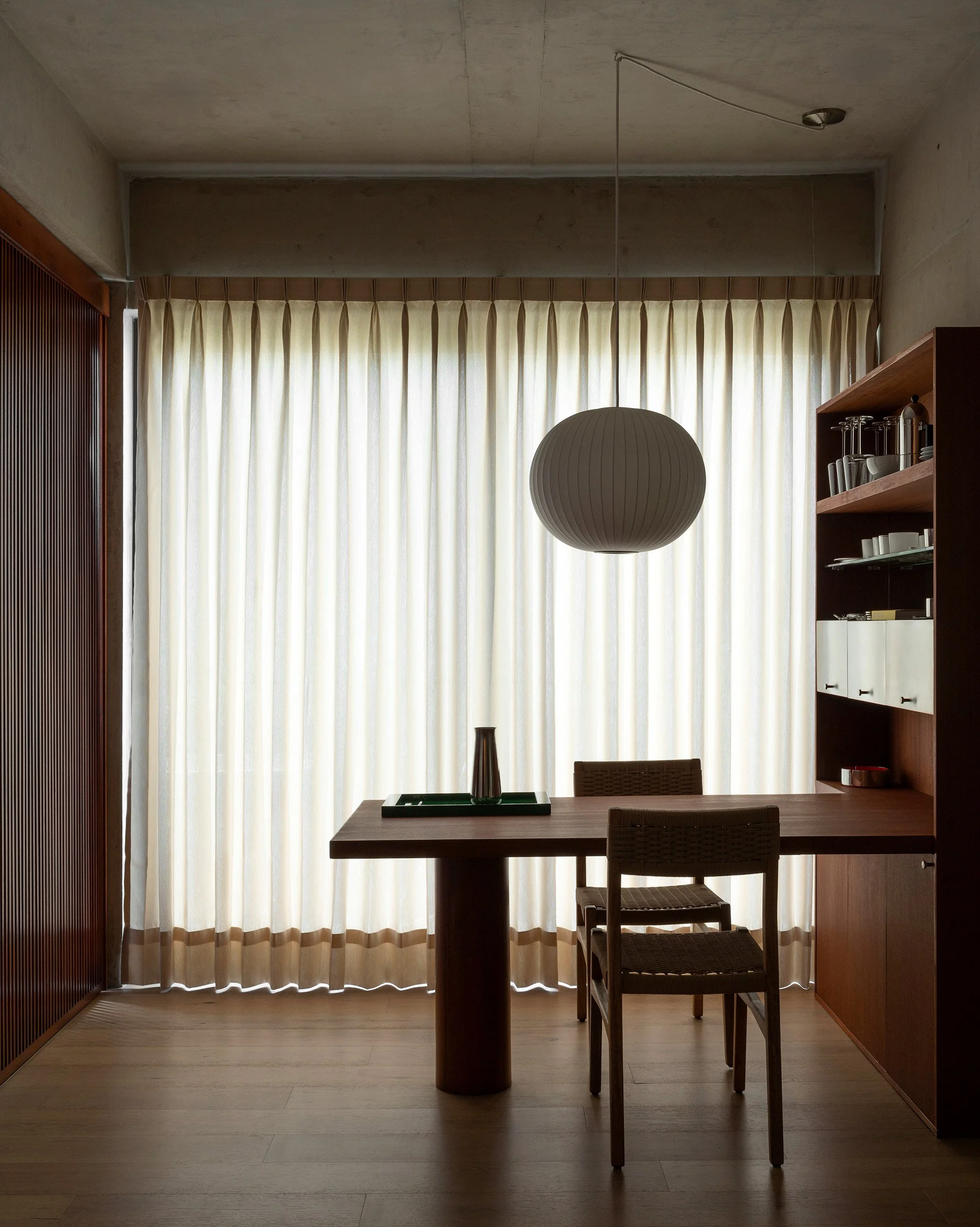 Bespoke dining area featuring woven chairs, an integrated wood pantry, and a sphere pendant lamp at San Luis Airbnb in Mexico City by Mariel Lozano Studio, photographed by Fabian Martinez.