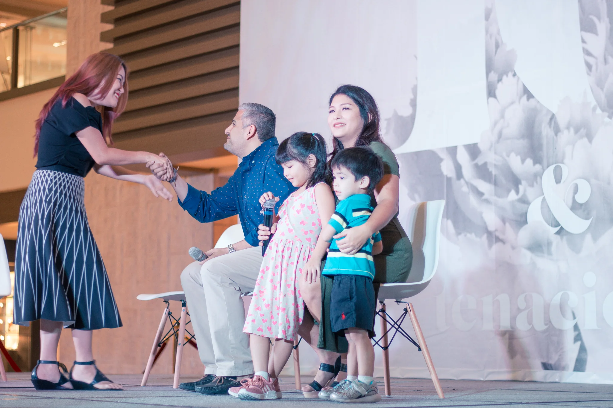 Andrea Amado is welcomed to the stage by Laveen Mirpuri. Theresa Carbonell sits on the right. literally juggling motherhood and business.