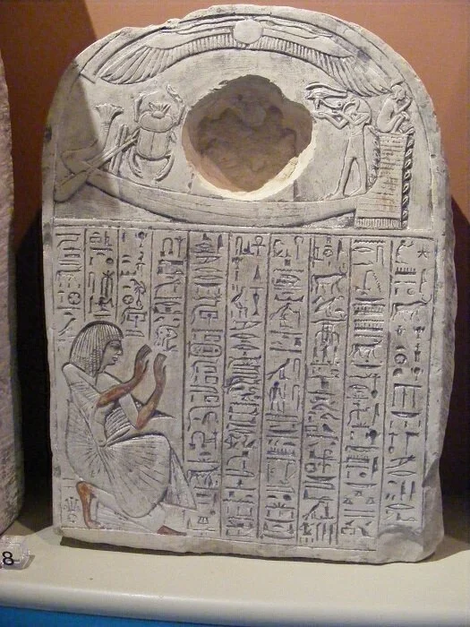 ‘In the boat, the sun is shown both as a child and sacred beetle (scarab). In the cavity, the sun was represented by a flint, now lost. The Ibis-headed god, Thoth, is offering the sacred eye of Horus. Below the scribe Ramose is shown offering a pray…