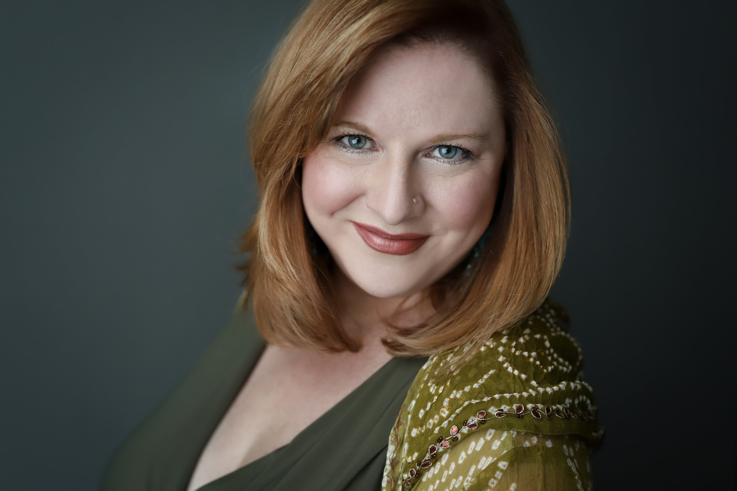 Smiling woman with red hair and green clothing in a studio portrait.