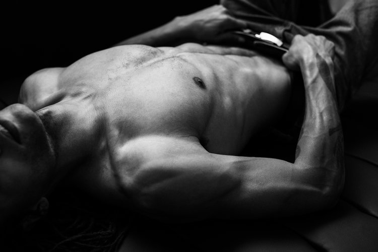 Black and white photo of a shirtless man lying down, focusing on muscular torso and arm.