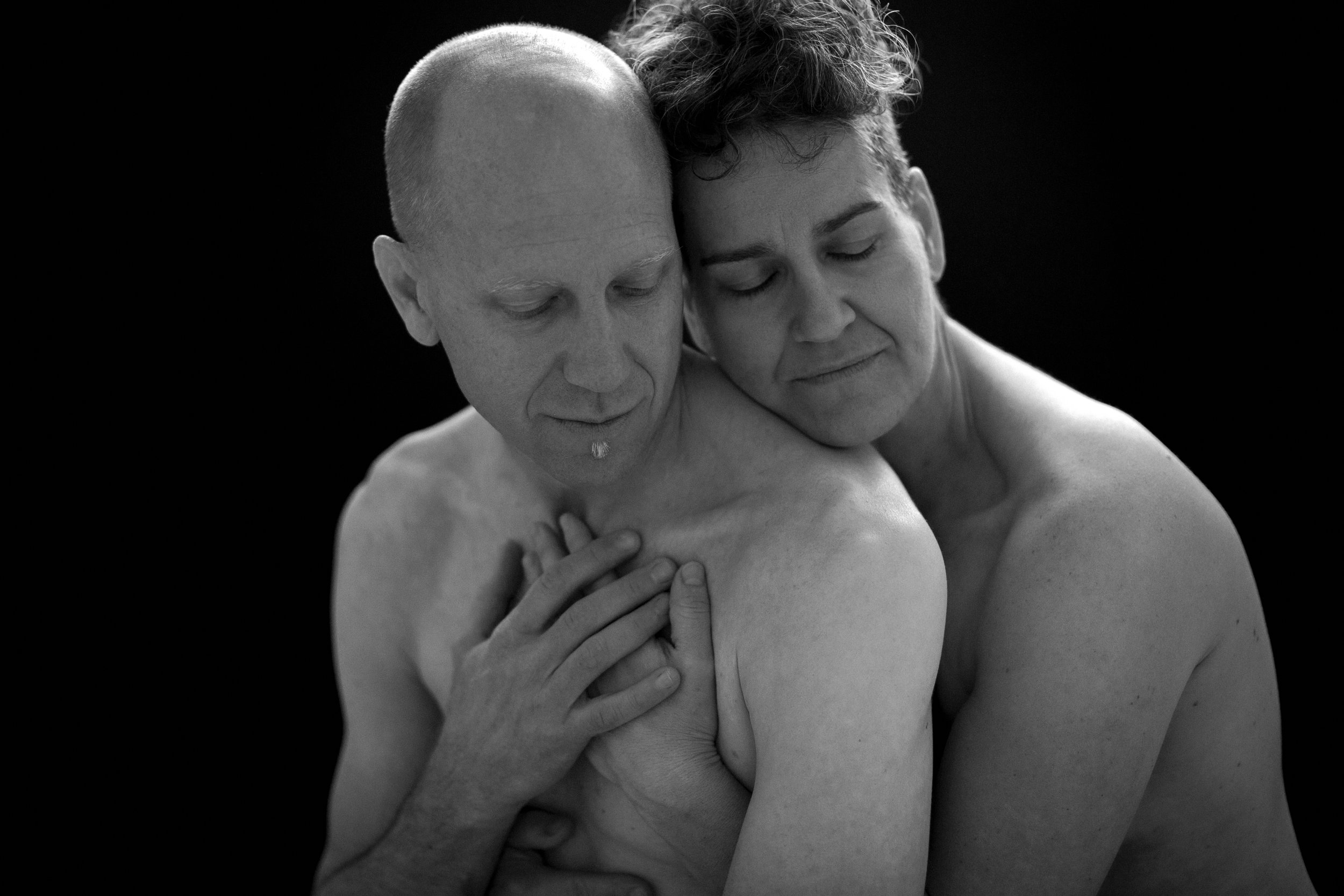 Black and white photo of two people embracing, with one resting their head on the other's back.