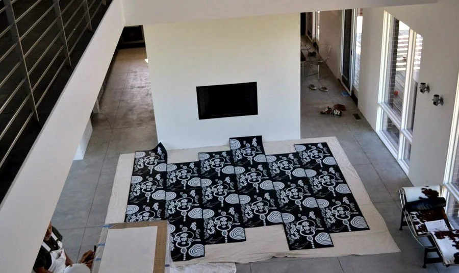 View of a modern living room with a black and white patterned rug, a wall-mounted fireplace, large windows, and some furniture and tools on the floor.