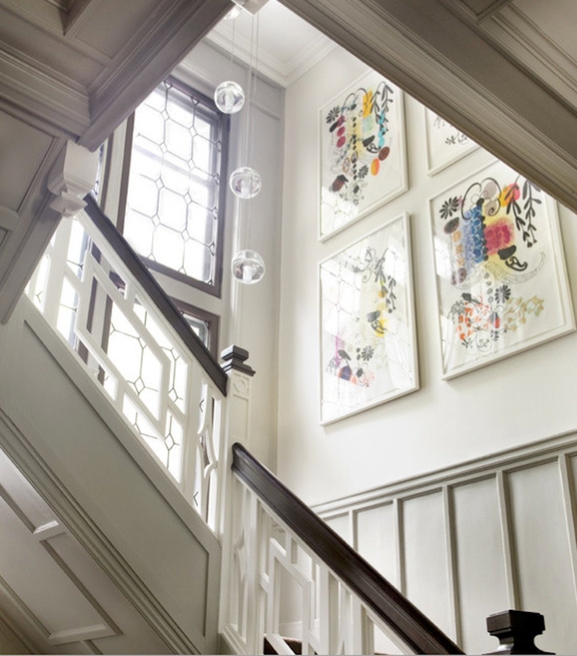Interior view of a staircase in a well-lit house with large windows, white-painted wood paneling, and colorful abstract artwork on the wall.
