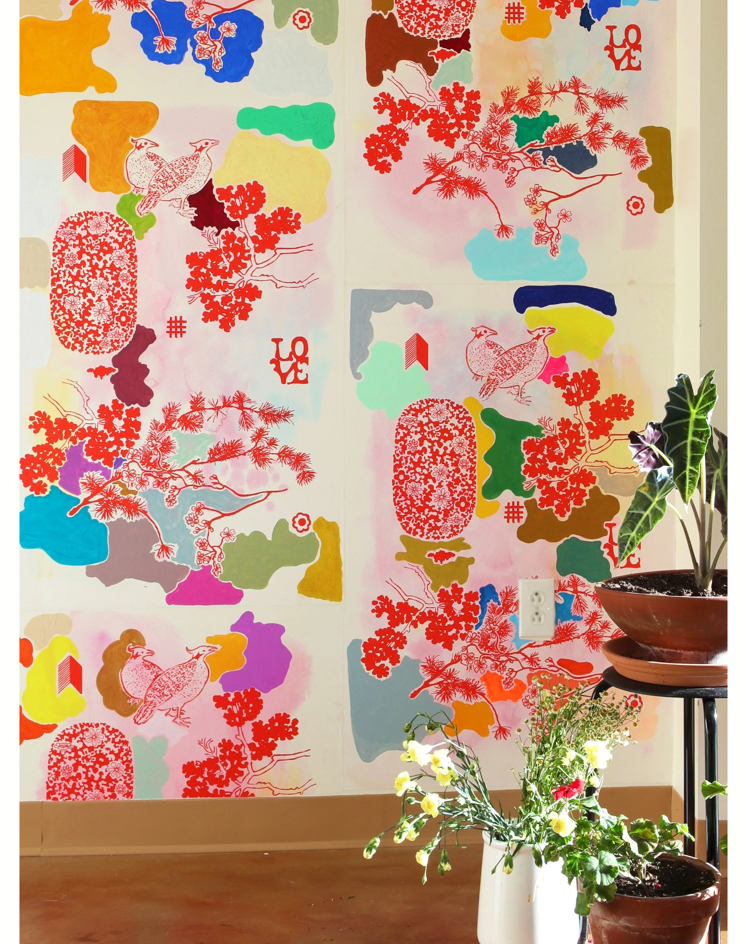 Colorful wall mural with various abstract shapes, red cherry blossoms, birds, the word 'LOVE' in red, and a plant in a white pot with yellow and red flowers in the foreground.