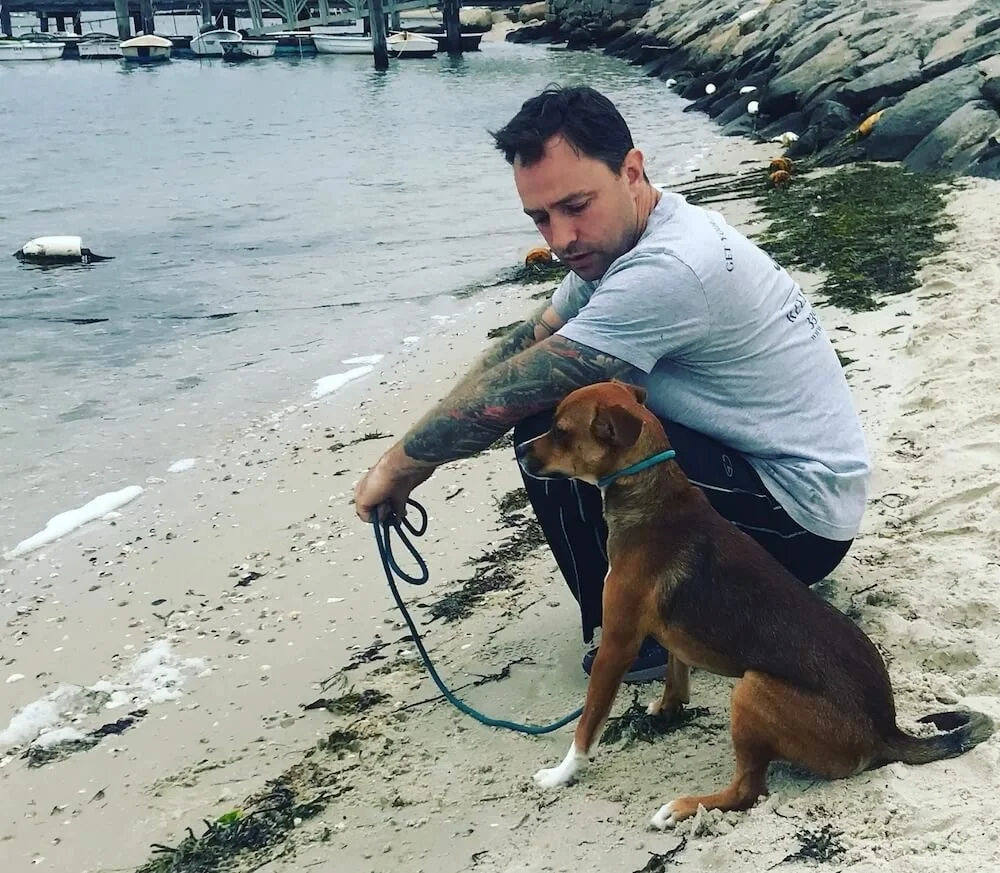 Lead trainer Ian sitting with a dog on the beach during a private lesson dog training session.