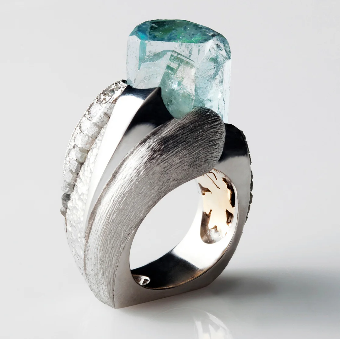 Taft Atkins: Sissy's Log Cabin Category III: 1st Place Palladium ring with a pierced 18k/yg “cave paintings” liner, a 27 carat raw-style aquamarine, raw cube diamonds and full cut diamonds.