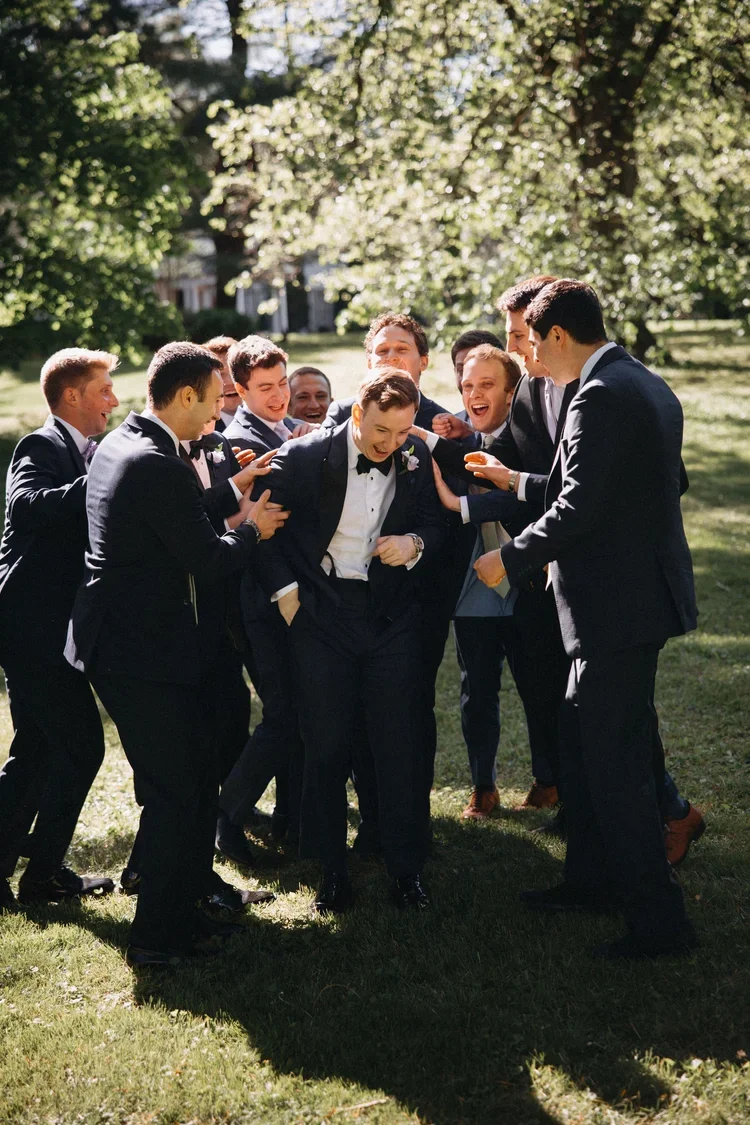 Groom laughs with his groomsmen outdoors as they gather together for a candid wedding day moment.