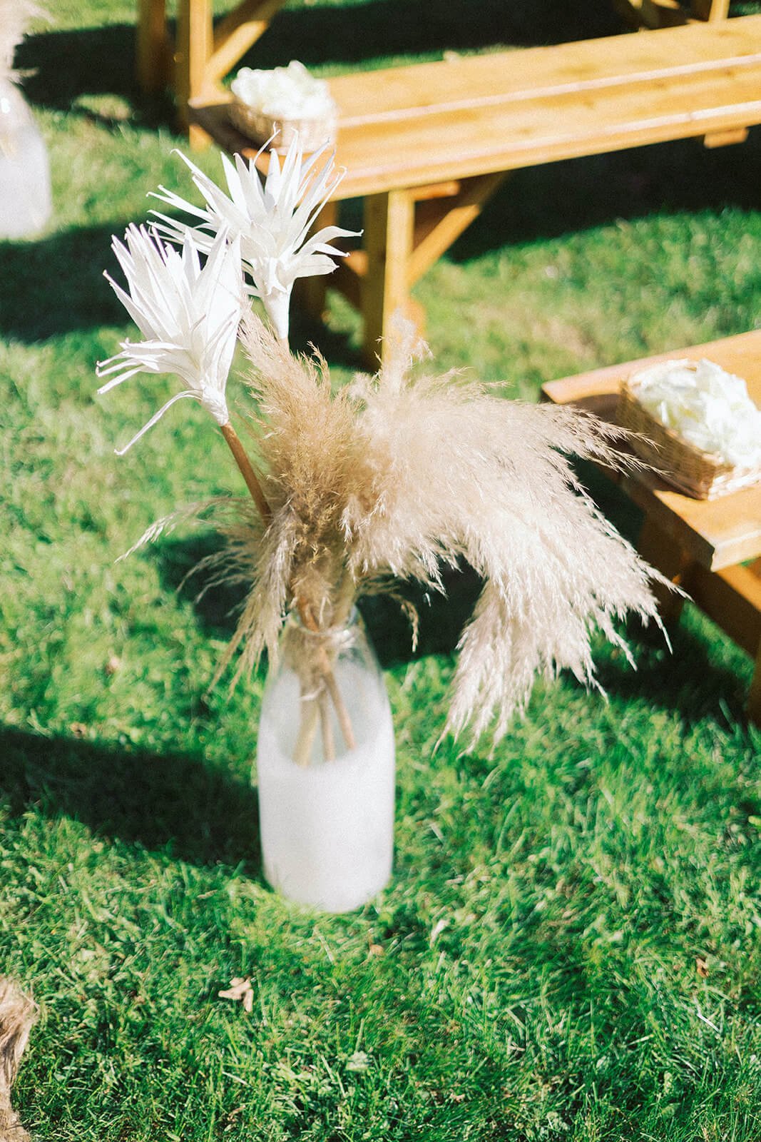 Rattan rugs and clear vases with pampas grass to decorate a boho outdoor wedding ceremony
