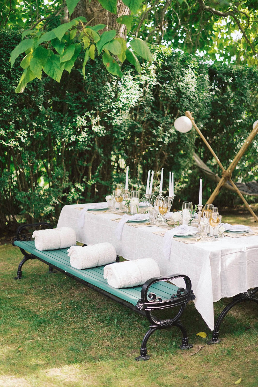 A long table with white linens and green and white cushions for a French picnic-style reception
