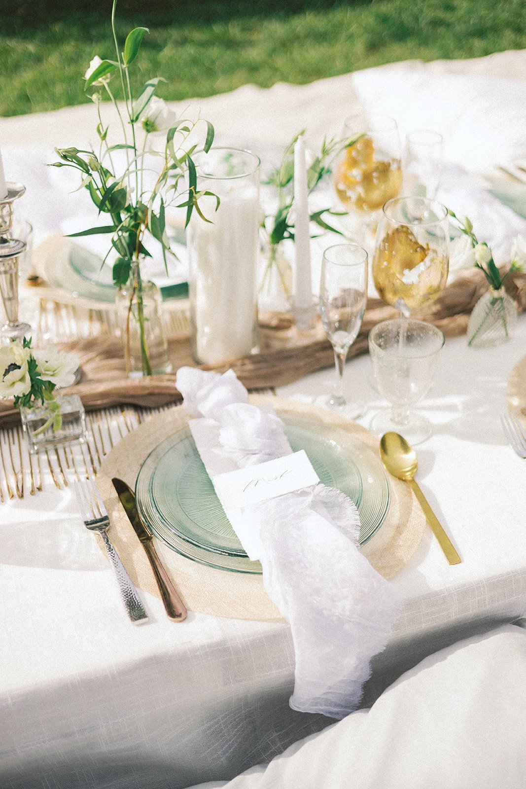 A long table with white linens and green and white cushions for a French picnic-style reception