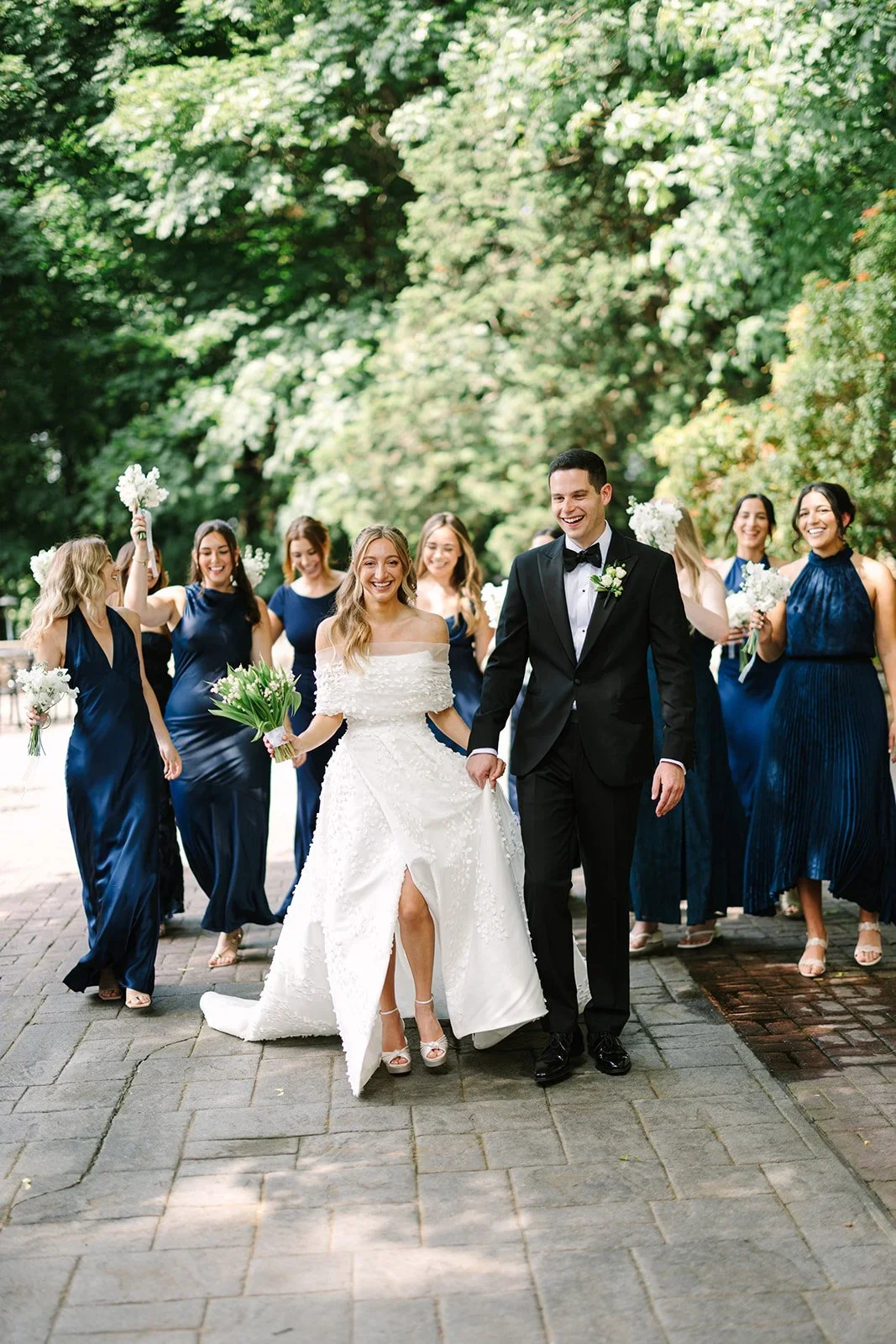 Bride and groom walking outdoors with their wedding party surrounded by summer greenery at a jewish wedding in New York
