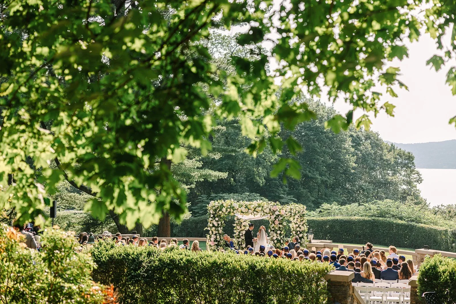 Wide view of the outdoor ceremony space with guests gathered beneath the trees