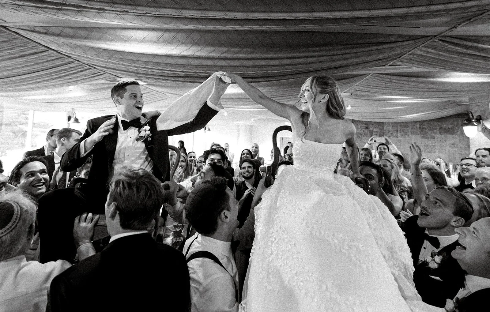 Bride and groom lifted high on chairs during the hora at a jewish wedding in New York