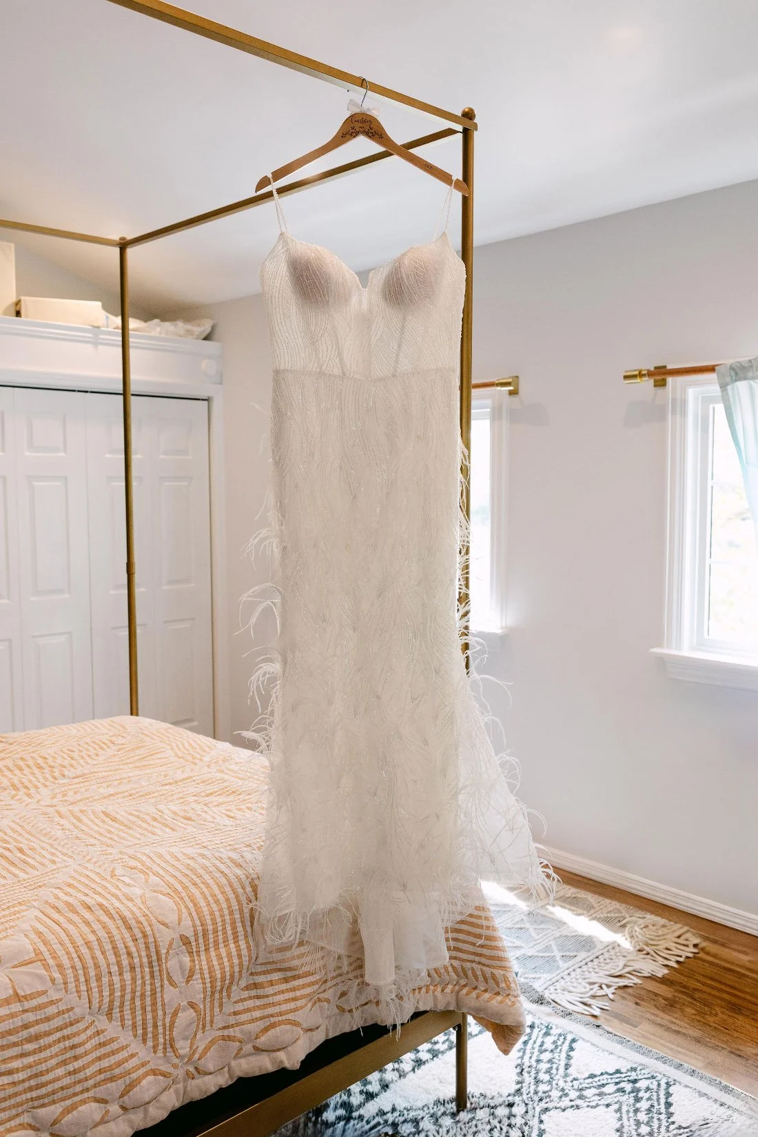 Feather-trimmed wedding dress hanging in bedroom before an outdoor wedding in New York