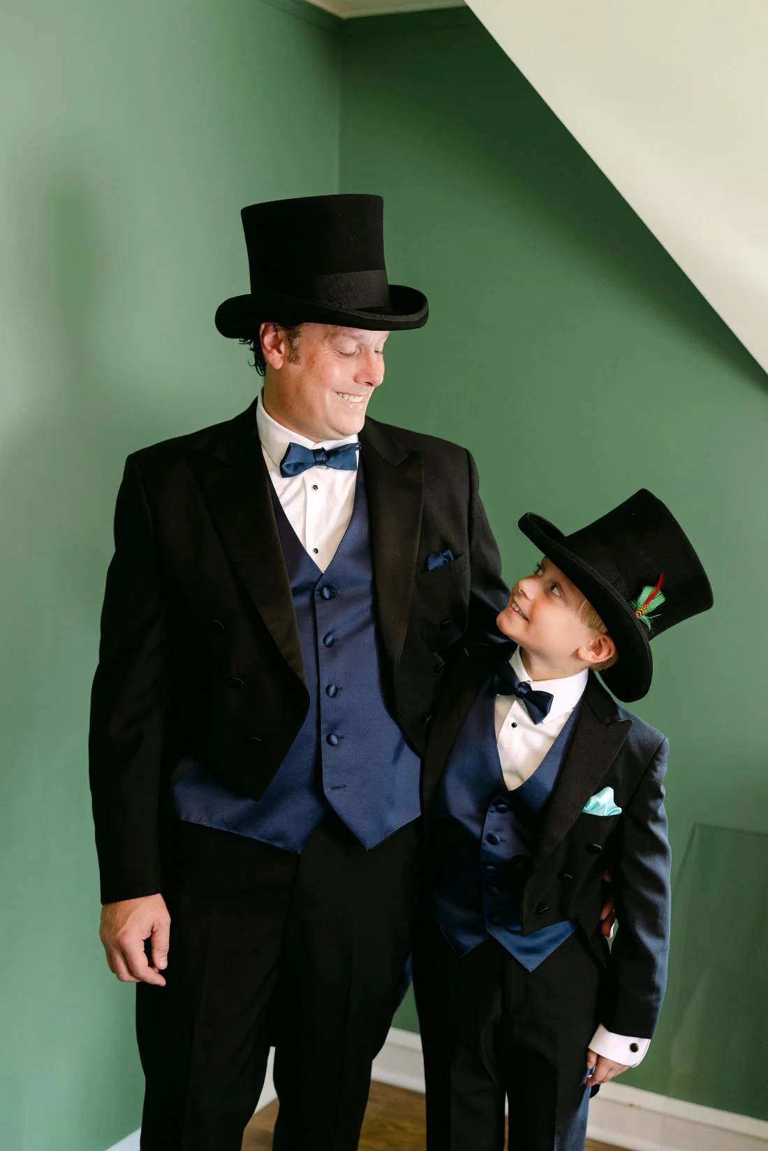 Groom and ring bearer sharing a moment in matching tuxedos and top hats before outdoor wedding in New York