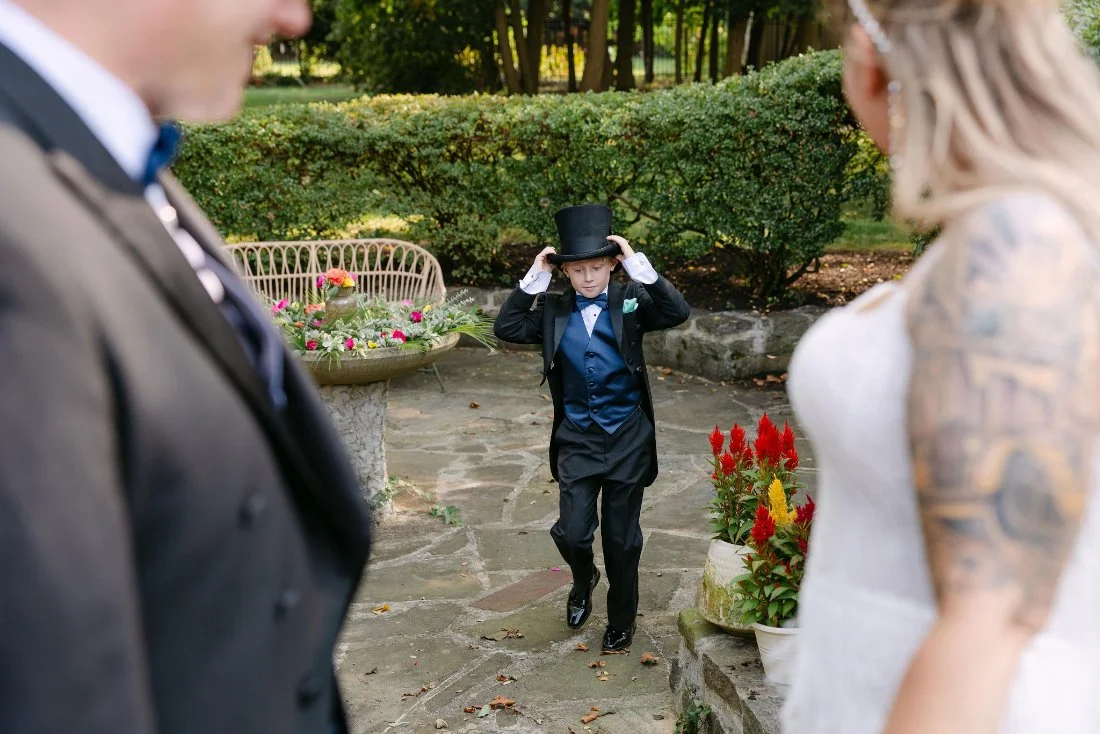 Ring bearer walking toward bride and groom in a matching tuxedo and top hat during outdoor wedding in New York