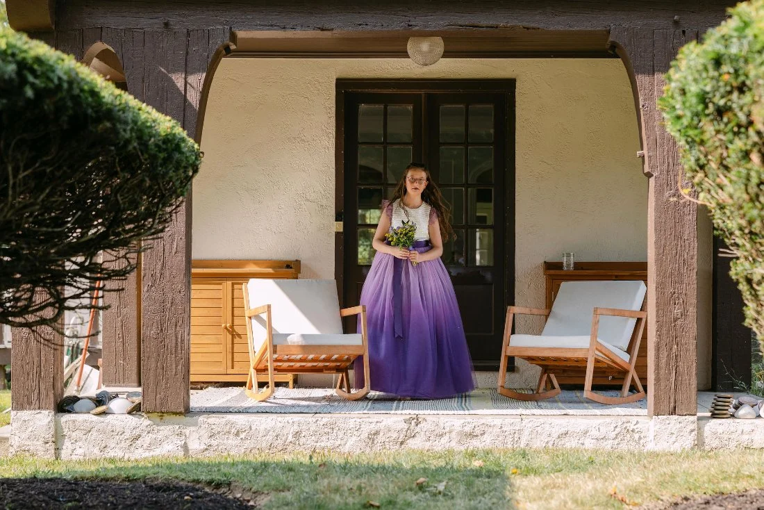 Flower girl walking out onto the porch holding a bouquet during an outdoor wedding in New York
