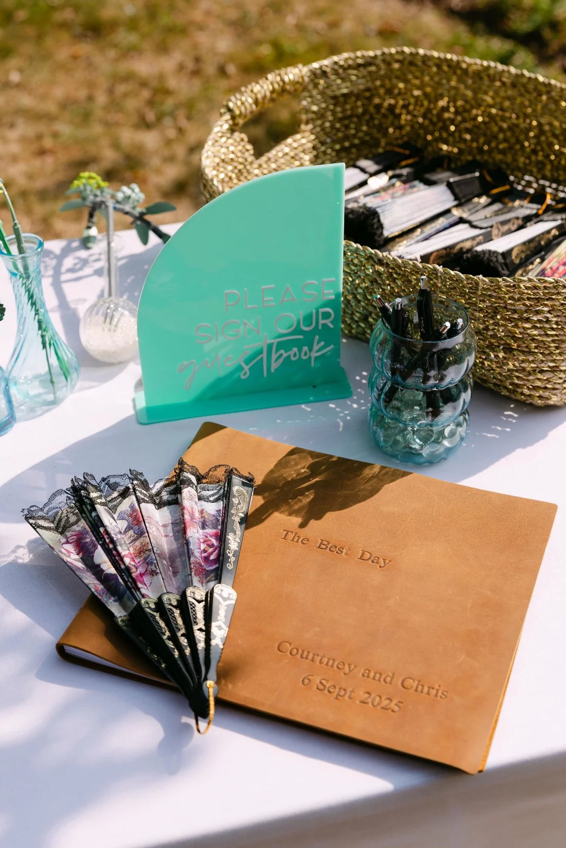 Guestbook table with fans, sign, and leather-bound journal for Courtney and Chris’s outdoor wedding in New York