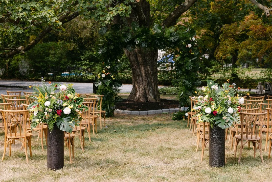 Outdoor ceremony setup with floral arrangements and wooden chairs under a tree in New York backyard wedding