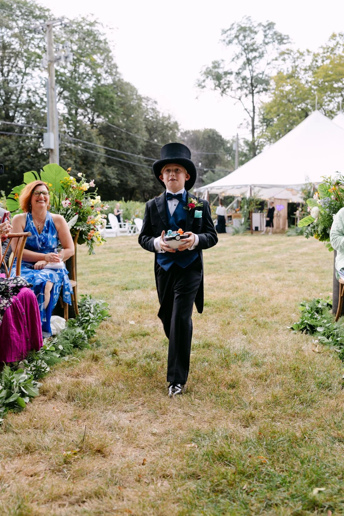 Ring bearer in top hat carrying a Pokémon-themed ring box down the aisle at an outdoor wedding in New York