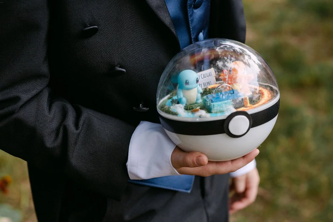 Custom Pokémon ring box with Squirtle and Charmander figures carried by ring bearer at outdoor wedding in New York