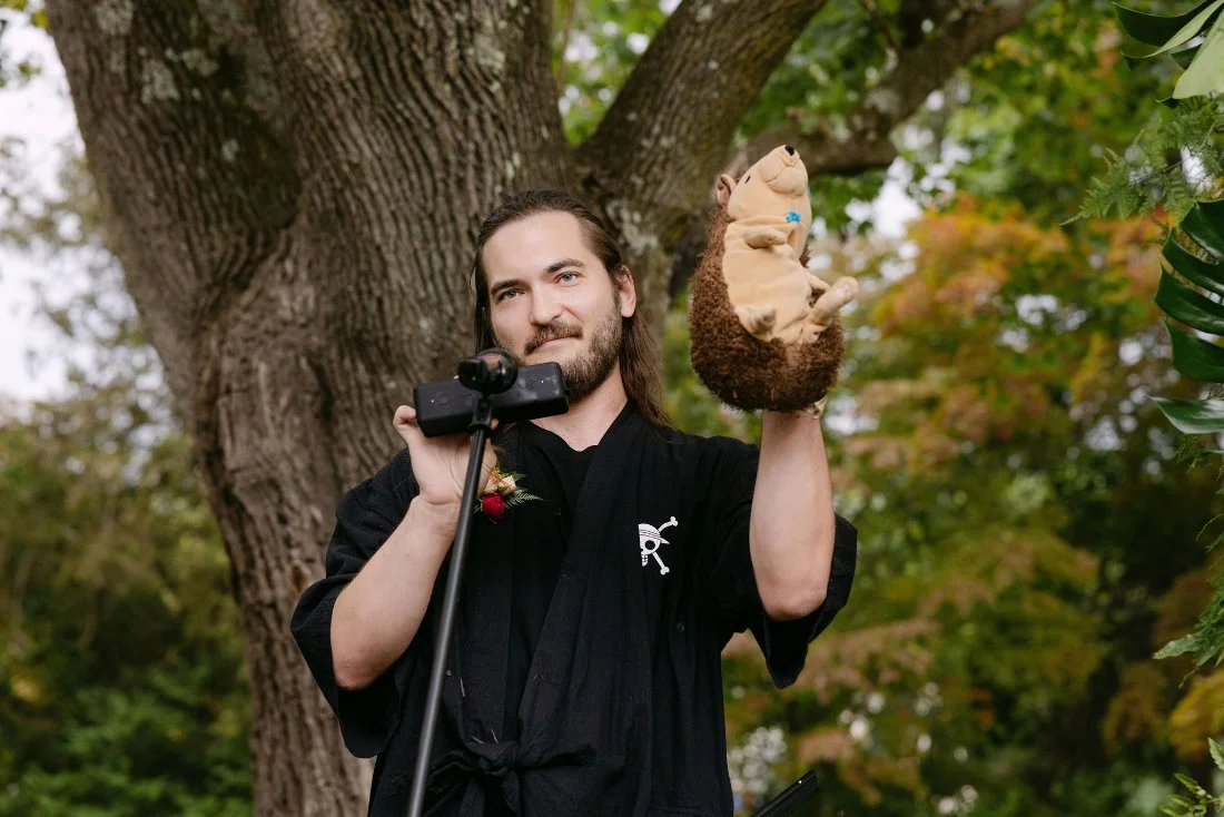 Wedding officiant holding a hedgehog puppet and microphone during outdoor wedding in New York