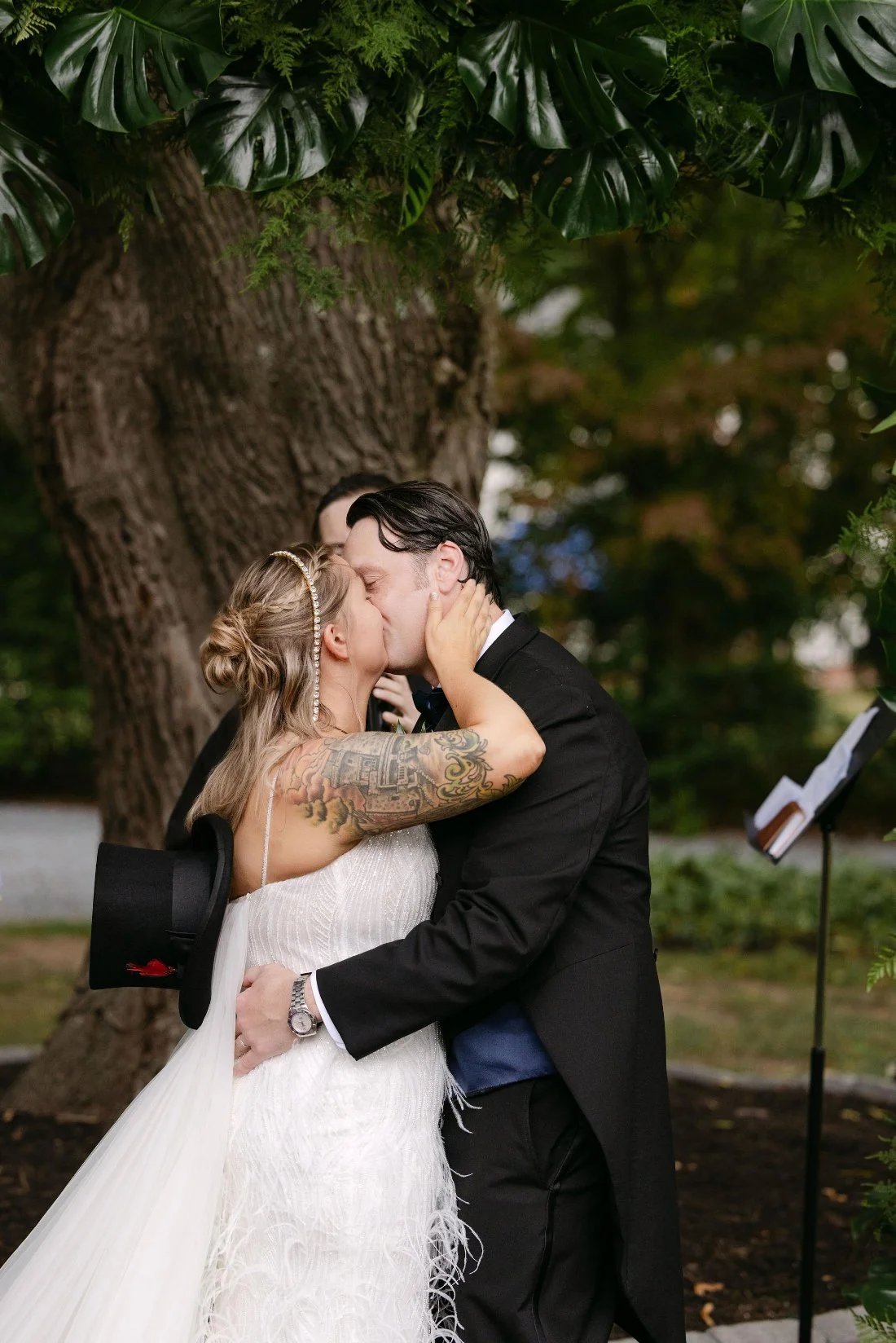 Bride and groom share their first kiss as newlyweds beneath a canopy of tropical greenery at their outdoor wedding in New York