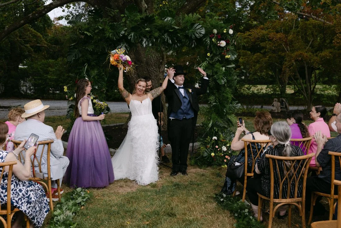 Just married! Couple celebrating joyfully under a floral arch after their outdoor wedding ceremony in New York