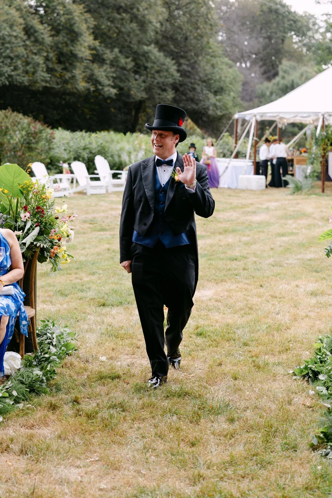 Groom waving to guests while walking down the aisle in a top hat at his outdoor wedding in New York