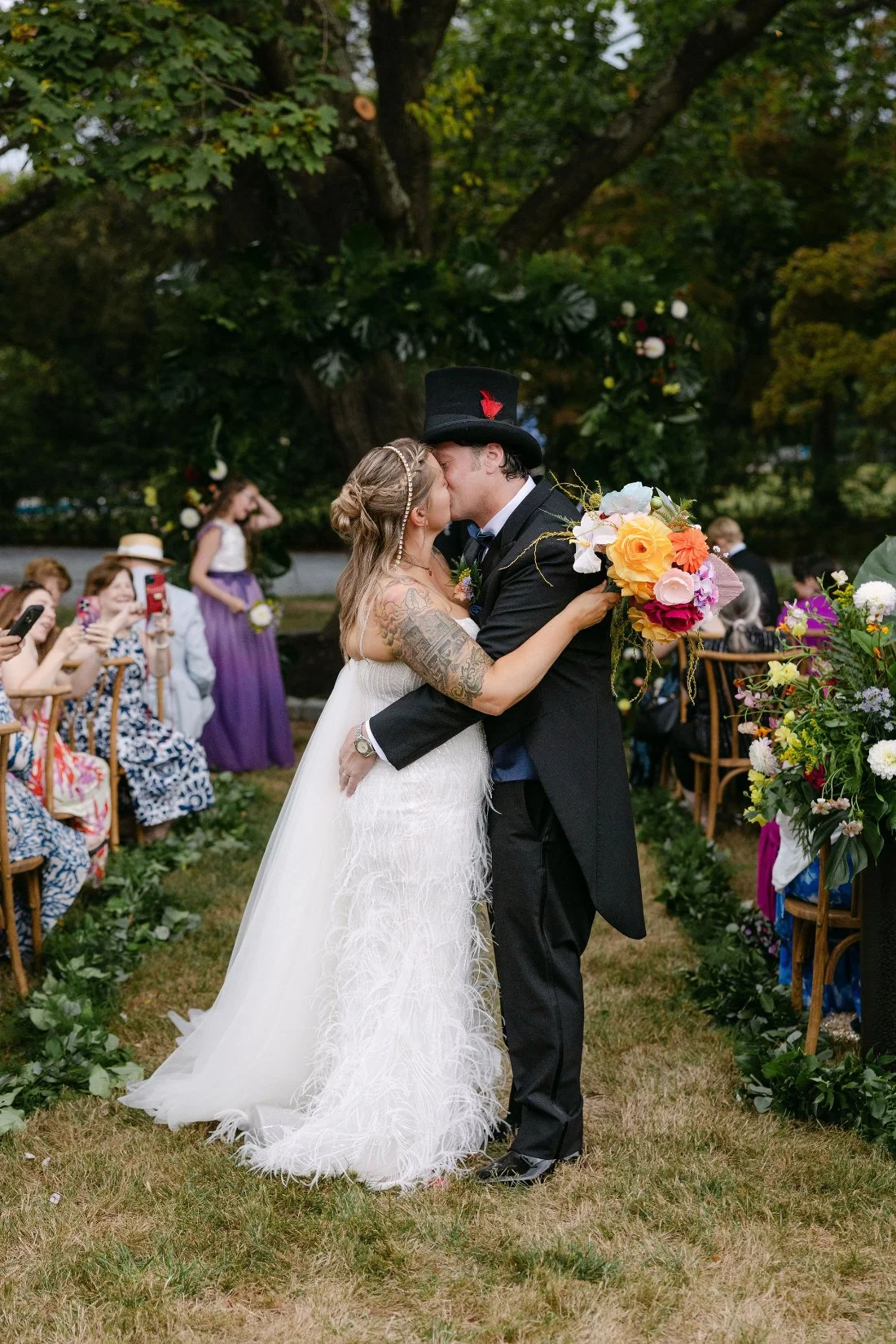 Bride and groom kiss during their joyful ceremony exit while holding a vibrant bouquet at their outdoor wedding in New York