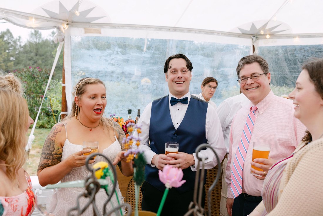 Bride and groom sharing drinks and laughs with guests during cocktail hour at their outdoor wedding in New York