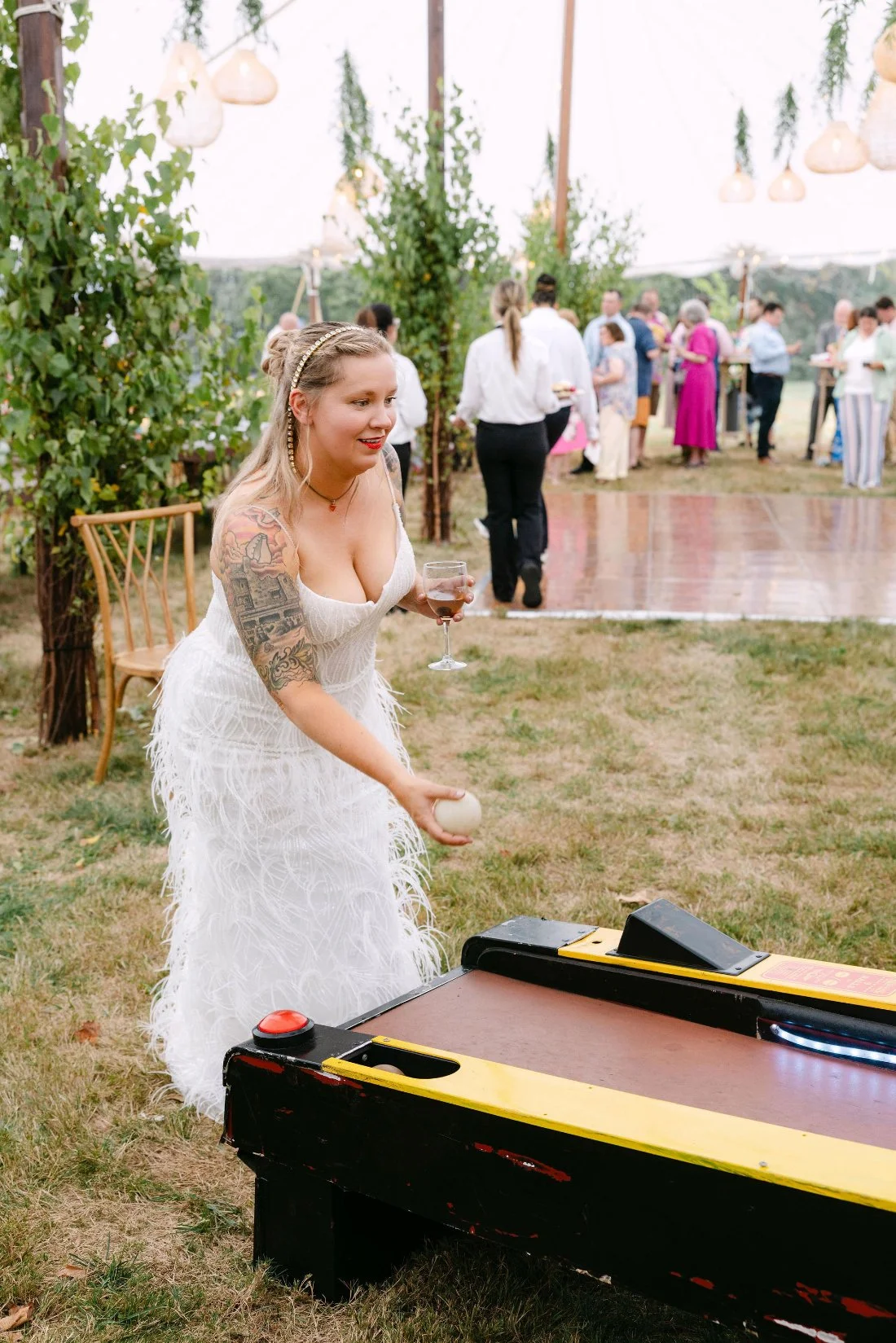 Bride playing skee-ball in her wedding dress during tented outdoor wedding in New York