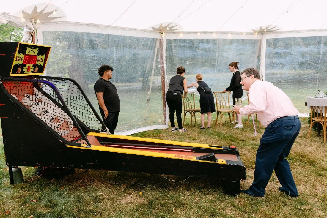 Wedding guest enjoying vintage skee-ball game during backyard outdoor wedding in New York
