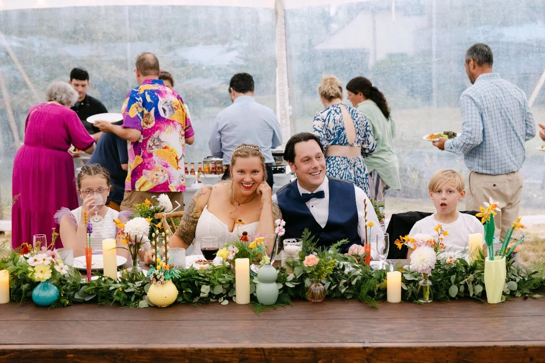 Bride and groom seated with their children at a vibrant head table during their outdoor wedding in New York