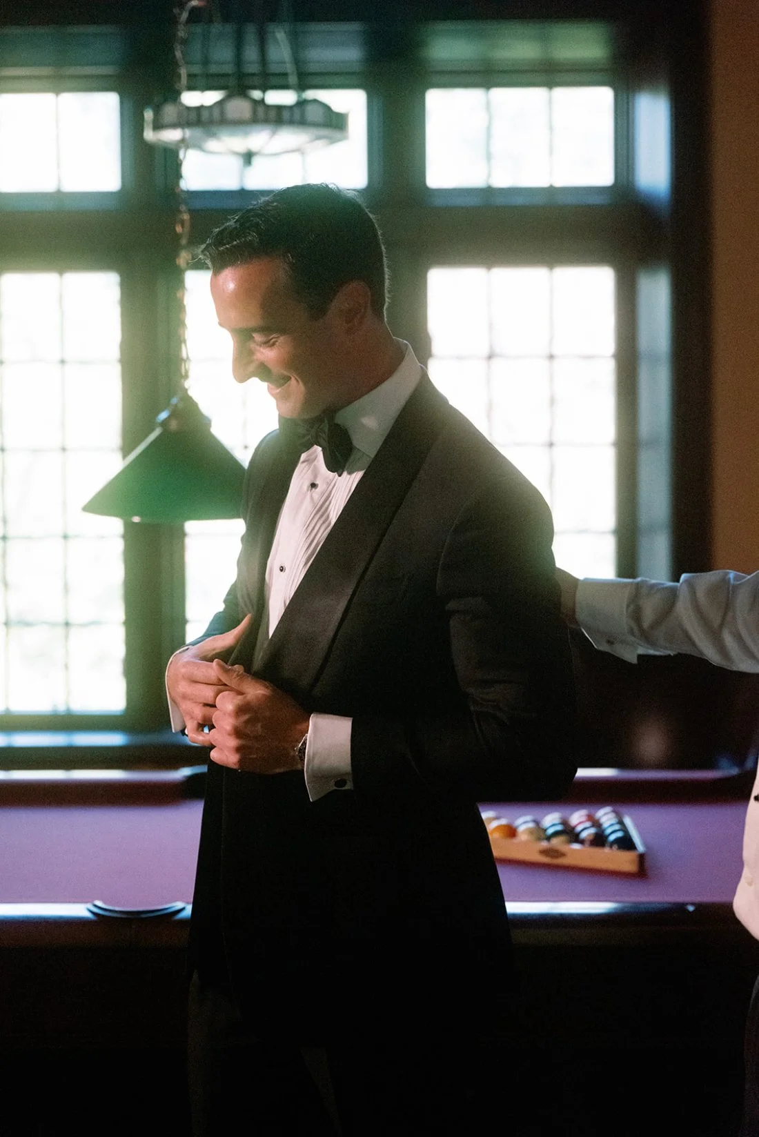 Groom portrait standing by a pool table inside the home during wedding preparations.