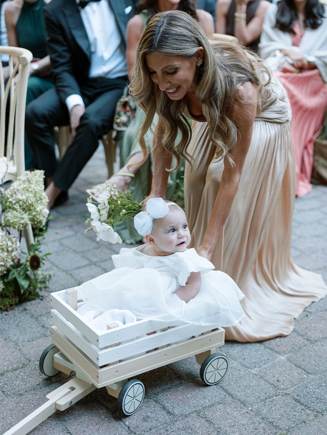 Little flower girl riding in a wagon down the aisle during a Hamptons wedding ceremony.