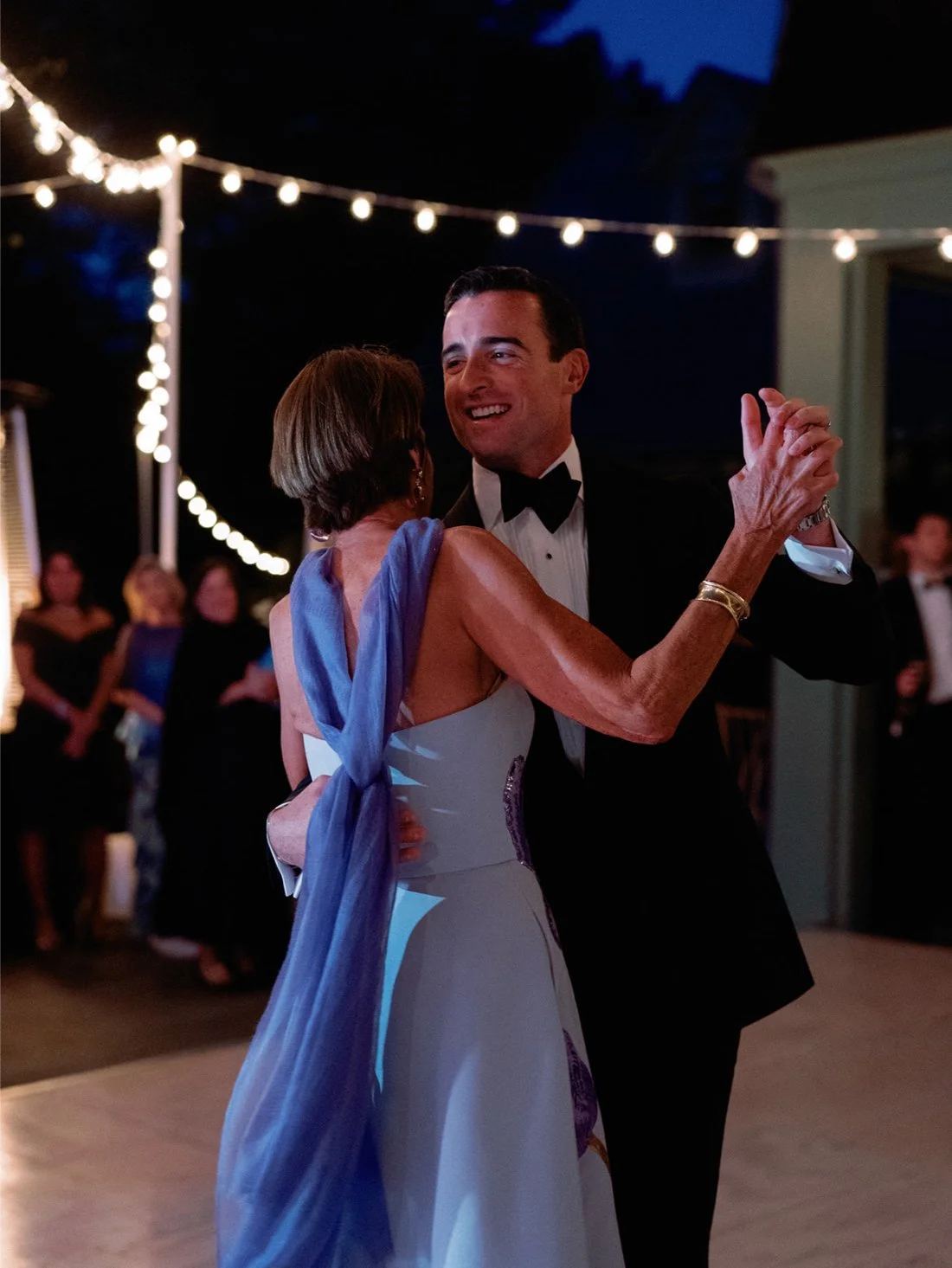Groom sharing a dance with his mother under the evening lights at their Hamptons wedding.