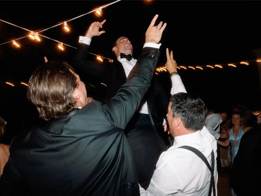 Groom being lifted into the air by friends and family during a joyful Hamptons wedding tradition.
