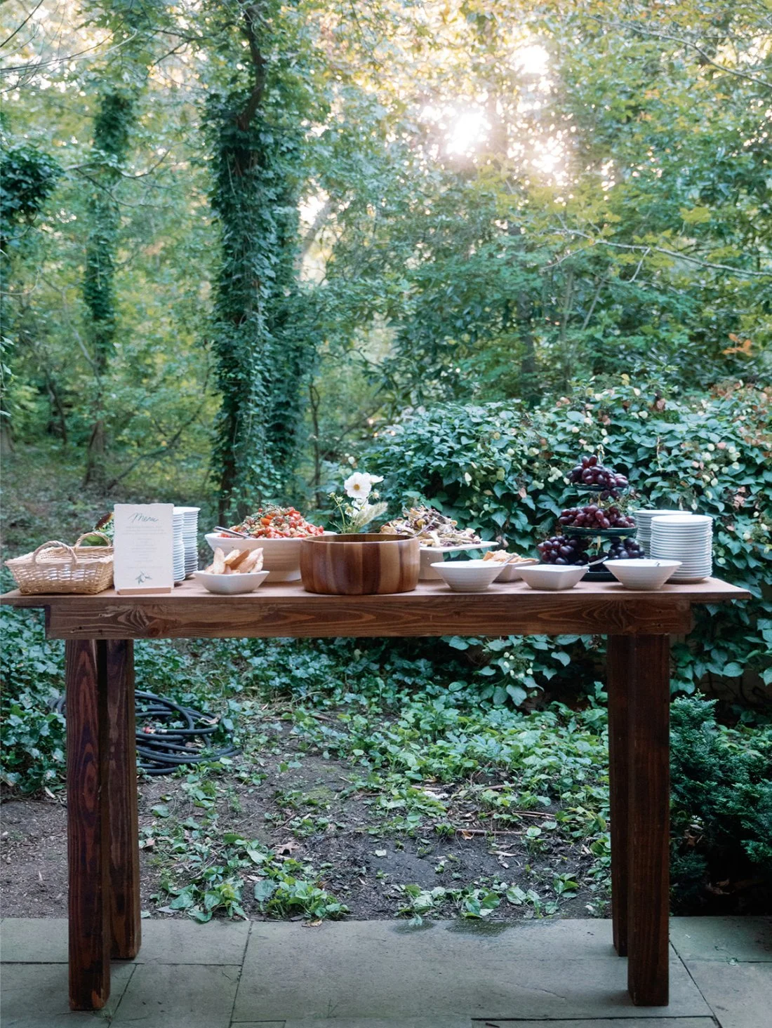 Wooden food display table set outdoors with fresh salads and grapes at a Hamptons wedding reception.