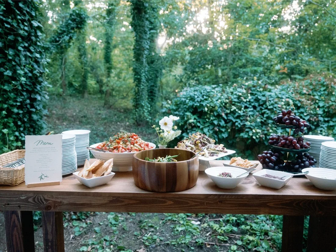 Mediterranean-inspired food station with stacked plates and fresh dishes at an outdoor Hamptons wedding.