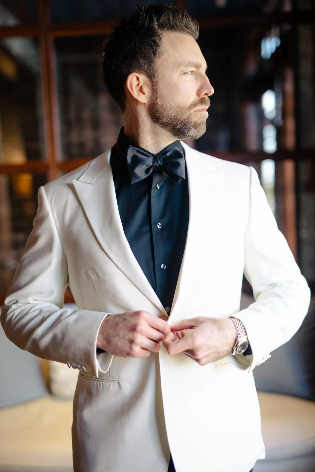 Groom getting ready in white dinner jacket and black bow tie by window light