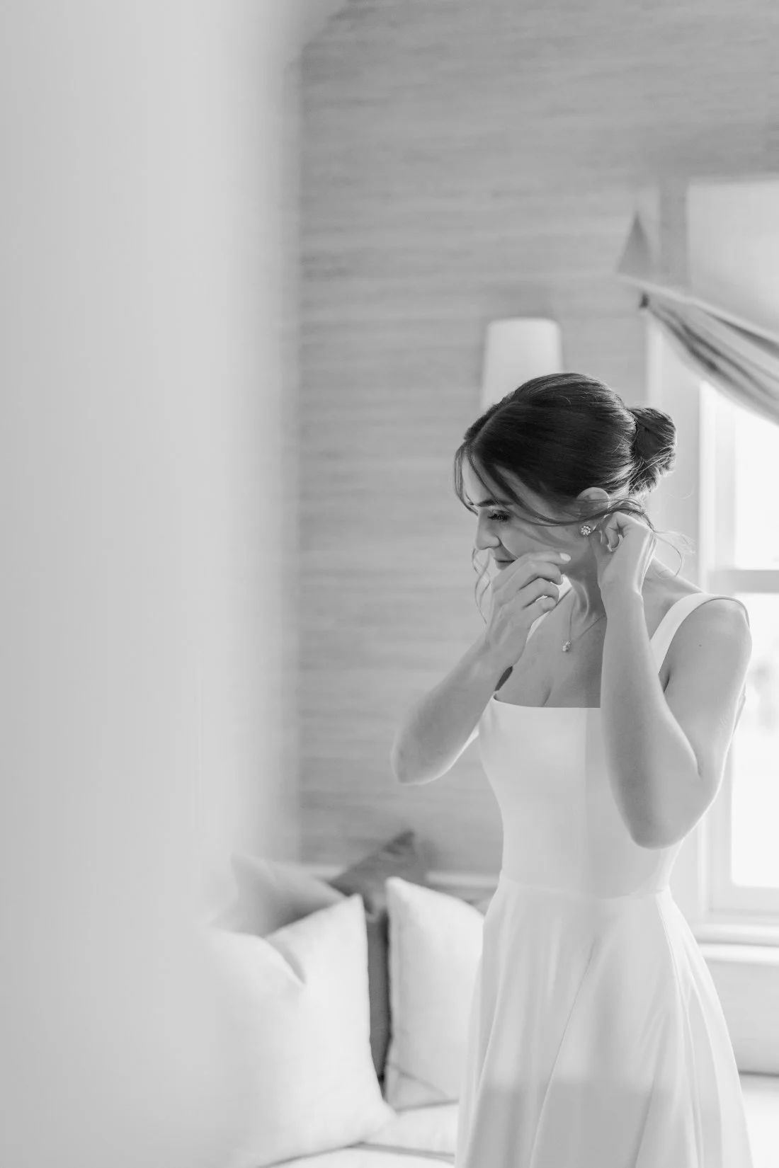Black and white photo of bride putting on earrings before ceremony