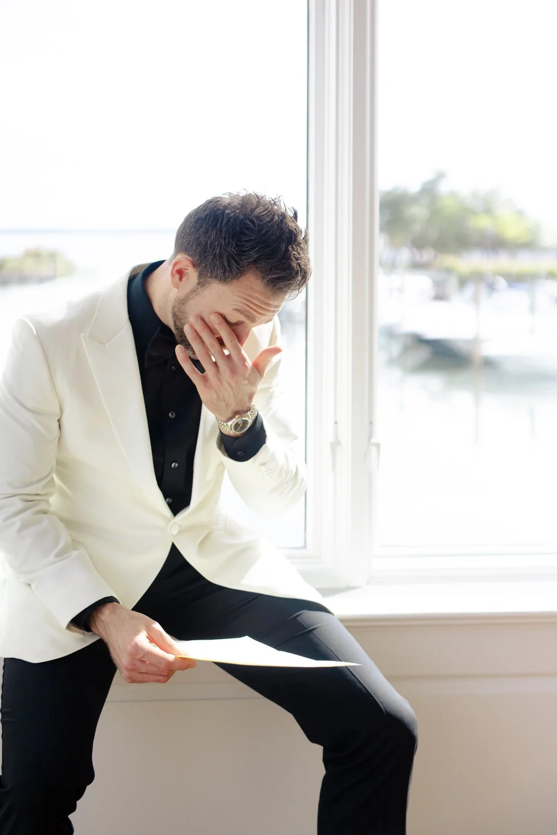 Groom reading emotional letter by window before Peconic Bay Yacht Club wedding