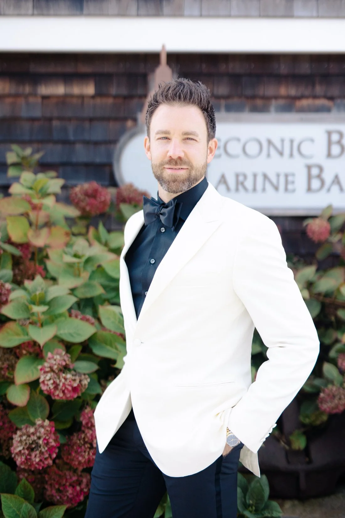 Groom portrait in white tuxedo jacket outside Peconic Bay Yacht Club with coastal florals