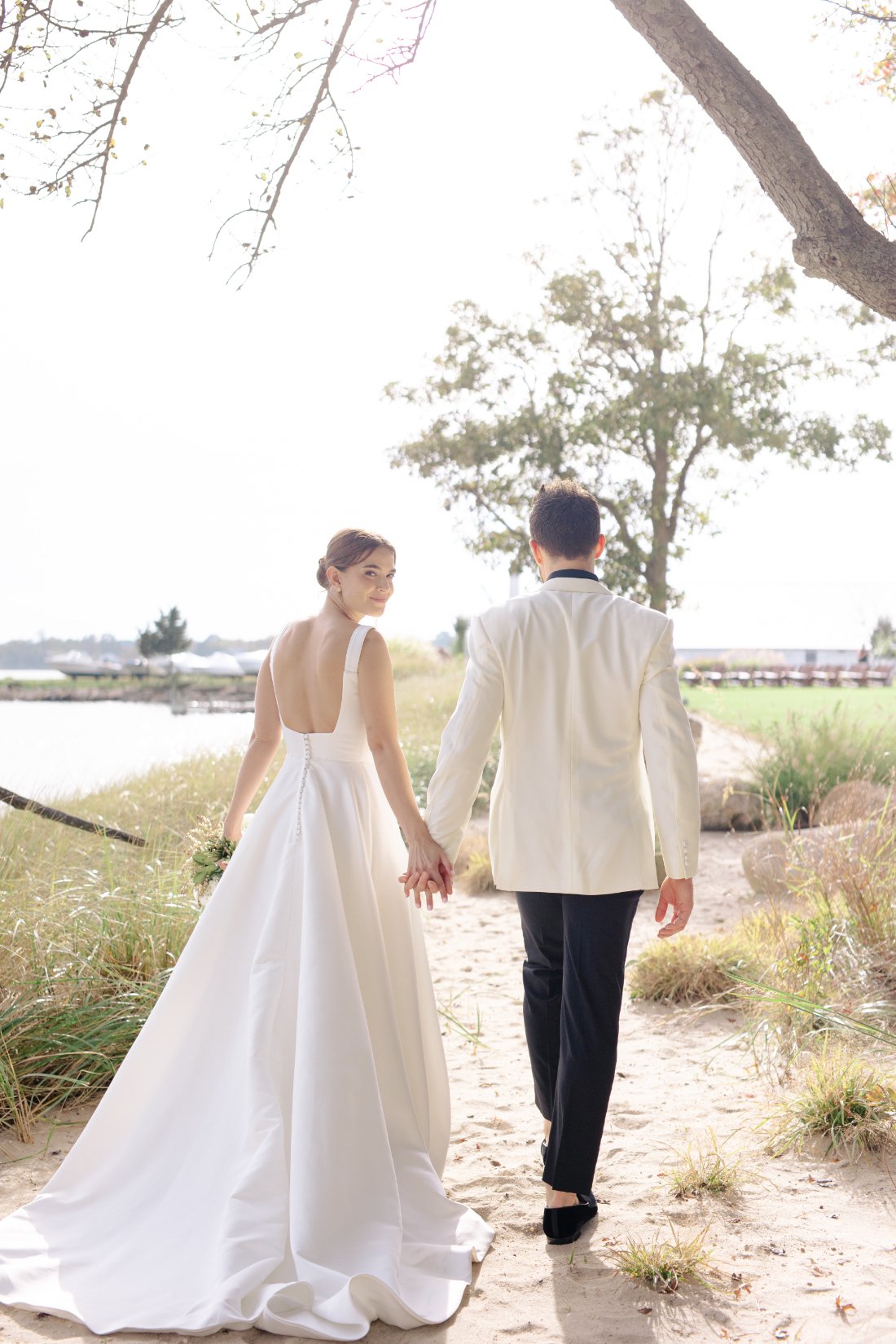 Bride and groom walking on beach during Peconic Bay Yacht Club wedding portraits